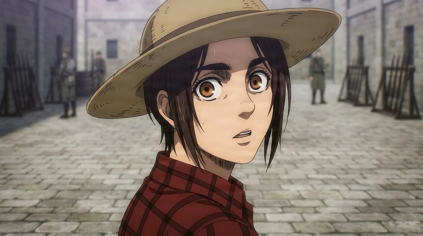 Gabi Braun, a young girl in a wide-brimmed hat and red plaid shirt, looks back wide-eyed in a stone courtyard with soldiers behind.