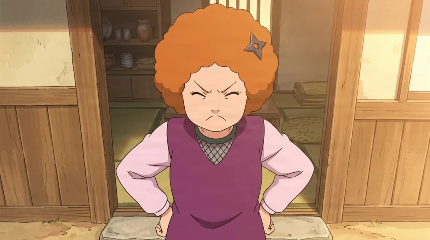 オレンジのアフロと手裏剣のかんざしをつけた年配の女性が、里の家の戸口で両手を腰に当て、厳しく顔をしかめている