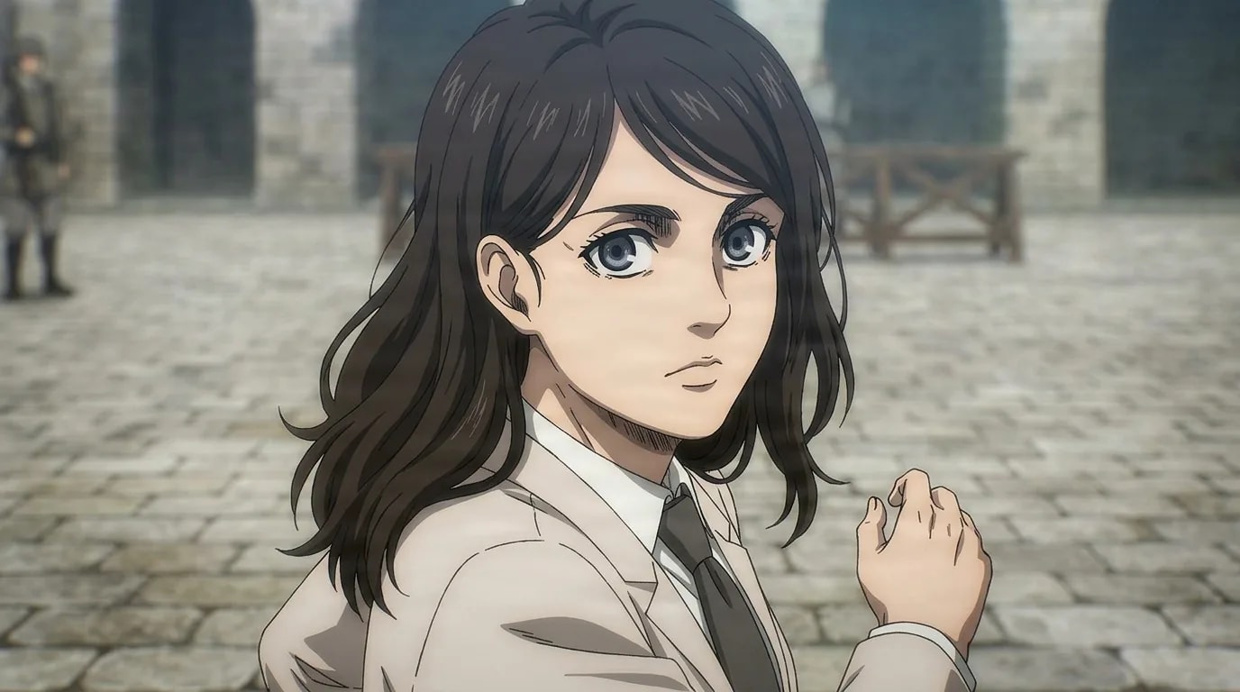 Cart Titan holder Pieck Finger looking back over her shoulder in a stone courtyard, long dark hair, pale jacket, shirt and tie.
